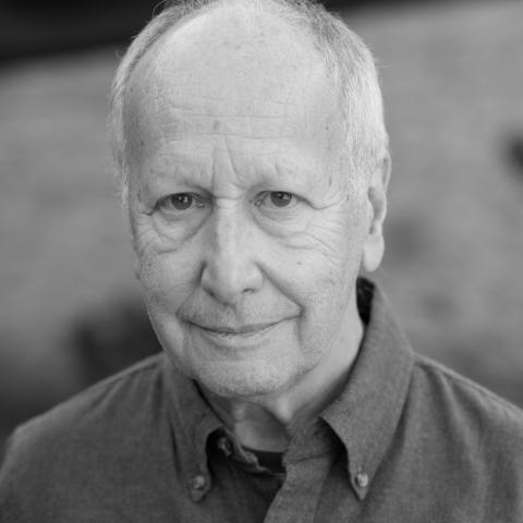A man smiling slightly, he is dressed in a dark shirt. The photo is in black and white. 